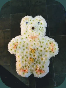 A teddy bear floral tribute in white and yellow flowers